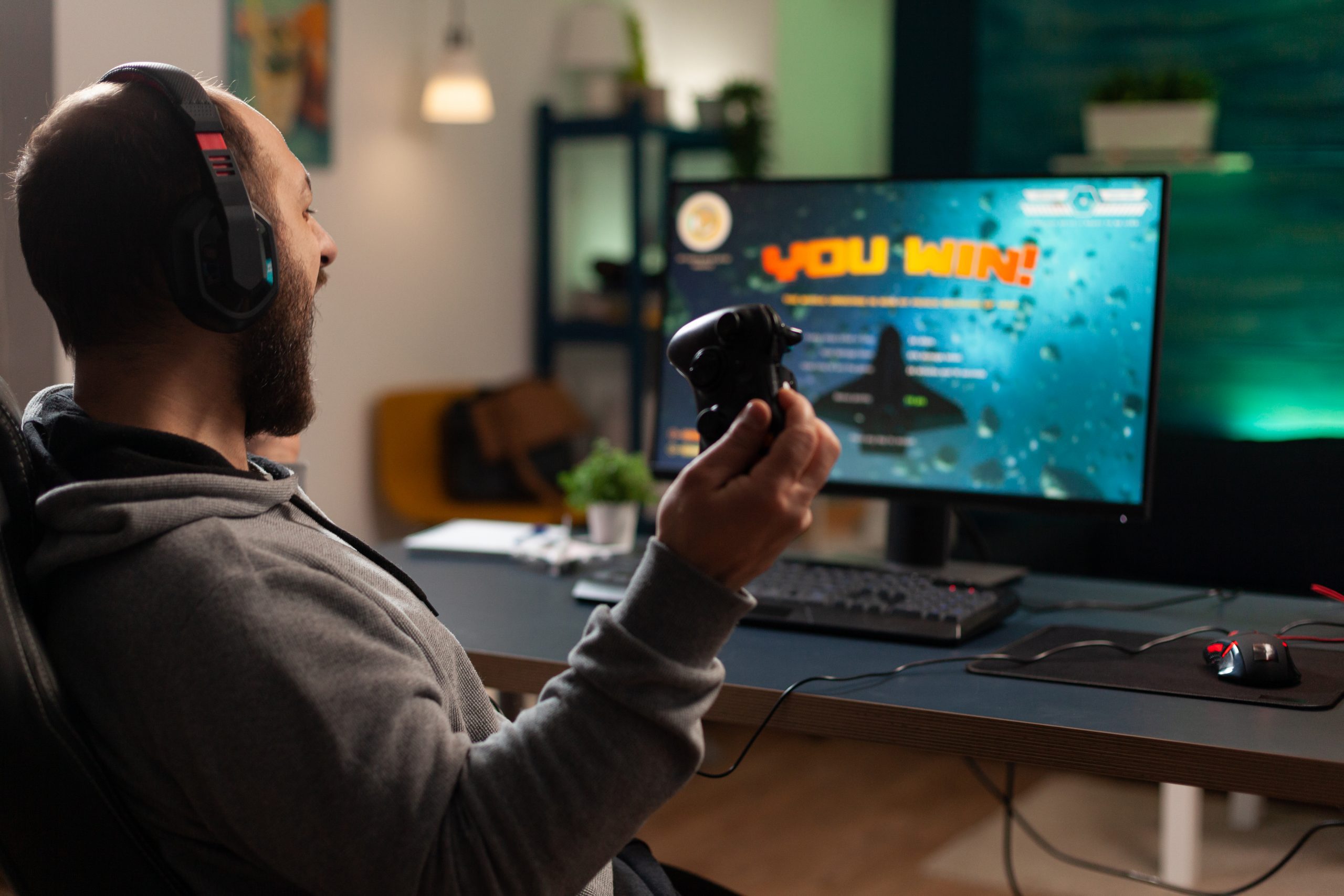 player winning video games with controller and headset in front of monitor man using joystick and headphones playing online games on computer person celebrating game win for leisure scaled