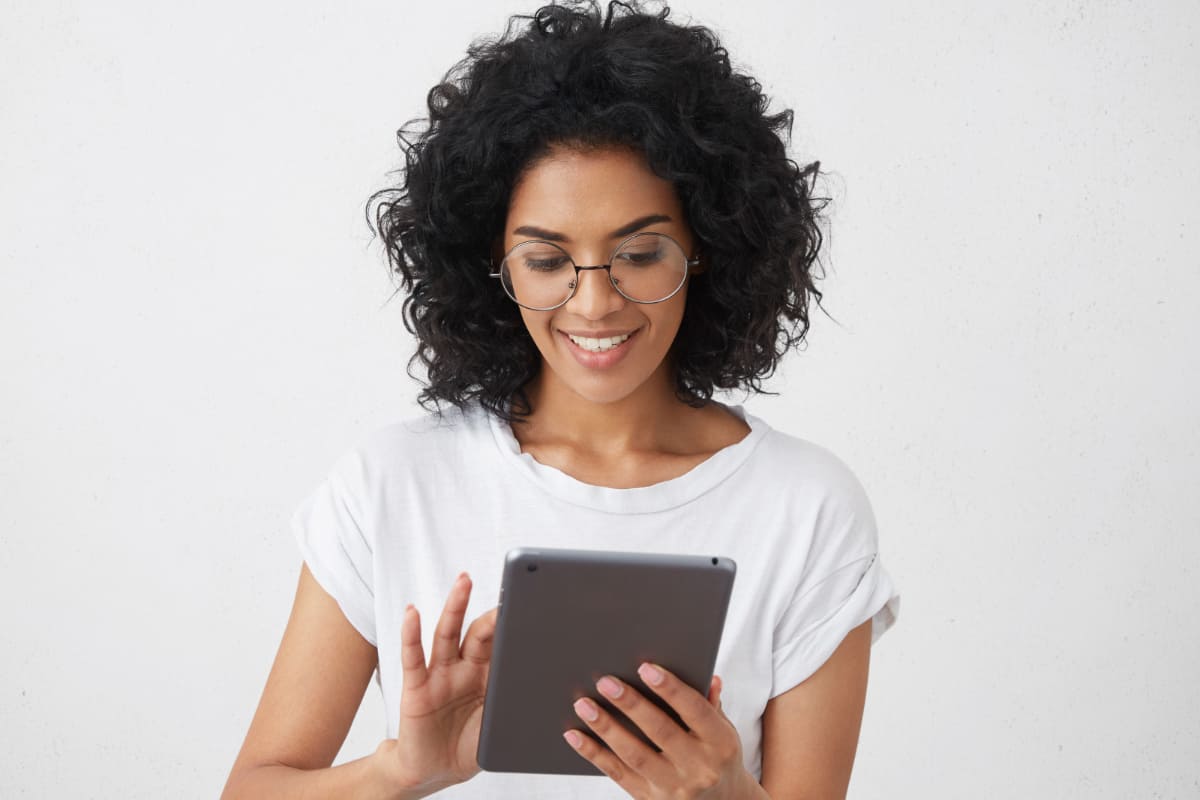 Mulher de pele escura, cabelos cacheados e óculos, usando um tablet