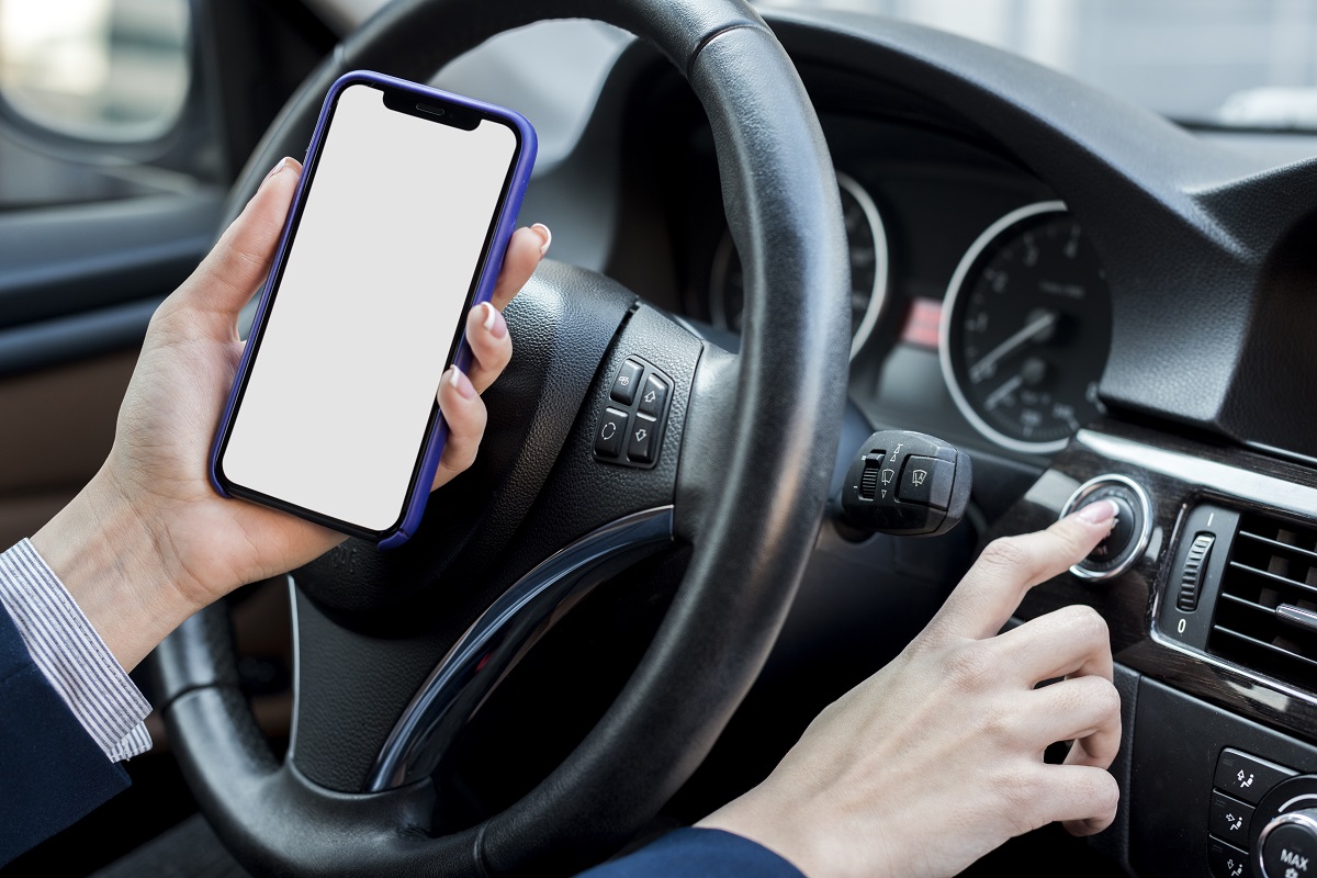 Mulher ao volante segurando um celular e apertando um botão no painel
