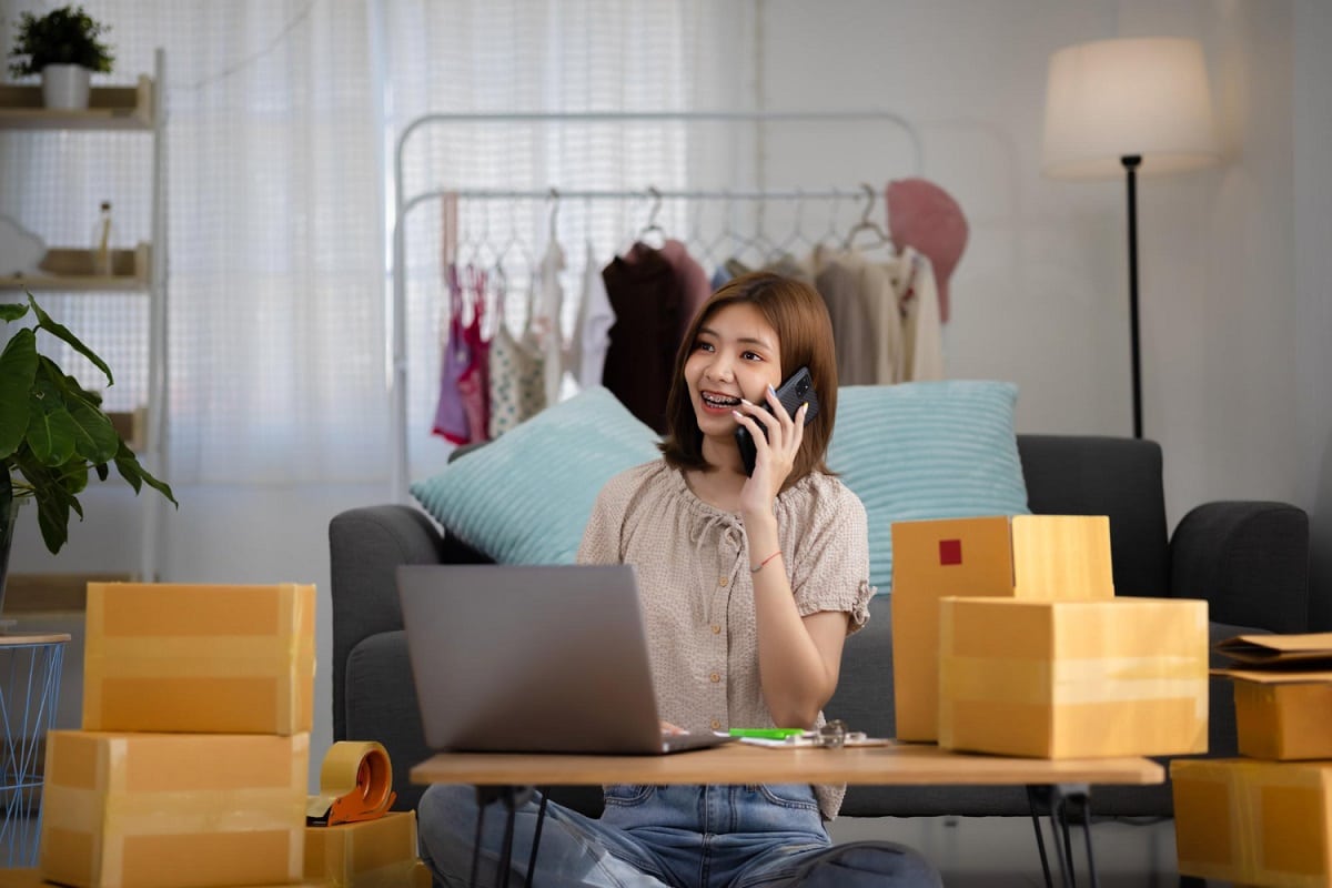 mulher jovem asiática falando no telefone com várias embalagens ao seu redor