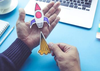 Mão segurando um foguete de papel, que faz alusão a Startups