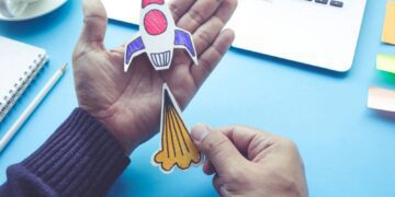 Mão segurando um foguete de papel, que faz alusão a Startups