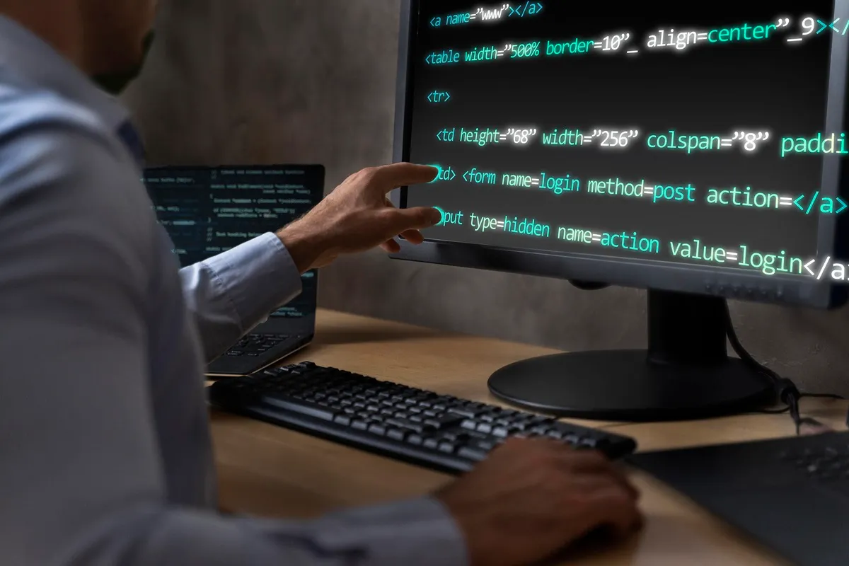Desenvolvedor de software trabalhando em um monitor com código HTML e CSS, ajustando elementos em uma interface de usuário.