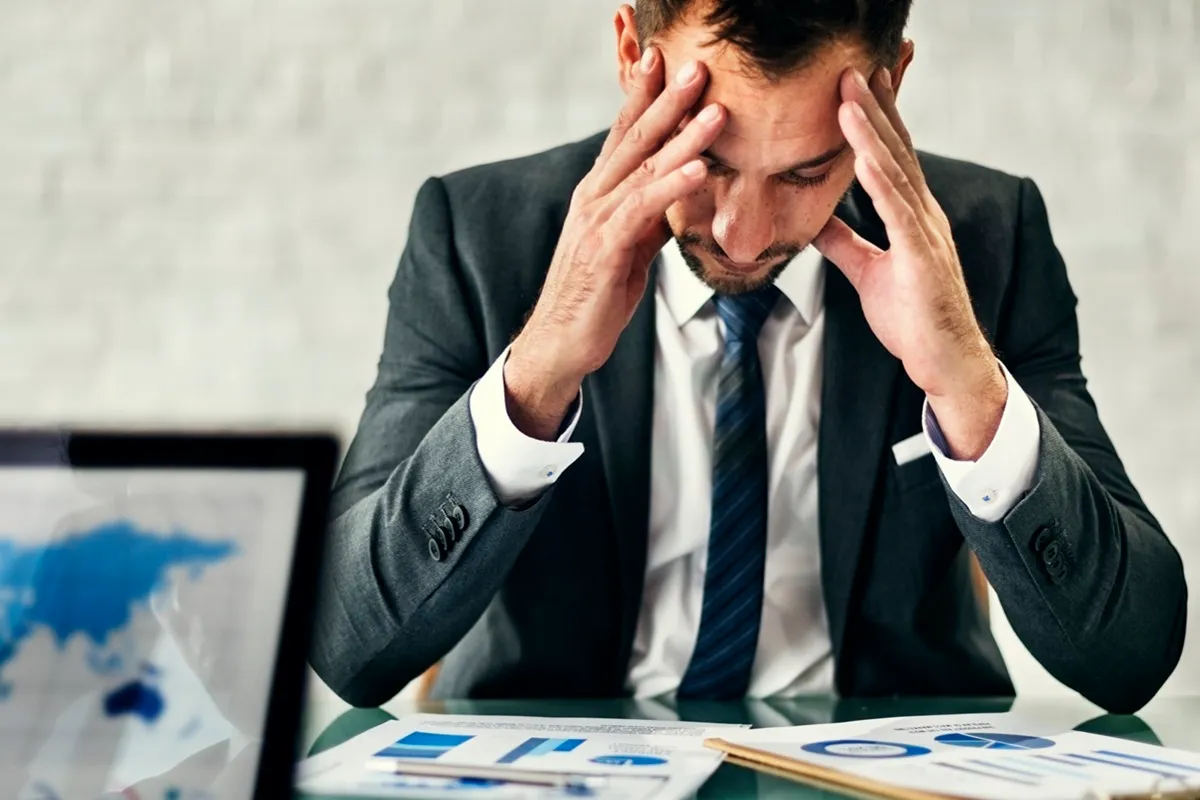 Homem de negócios preocupado com as mãos na cabeça, analisando gráficos financeiros no escritório.