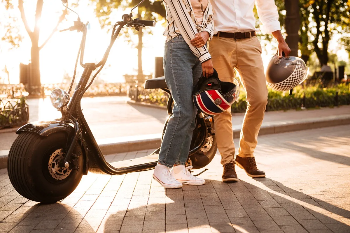 Tecnologias inovadoras em motocicletas elétricas 29 Casal segurando capacetes ao lado de uma motocicleta elétrica preta em um ambiente urbano ao pôr do sol.