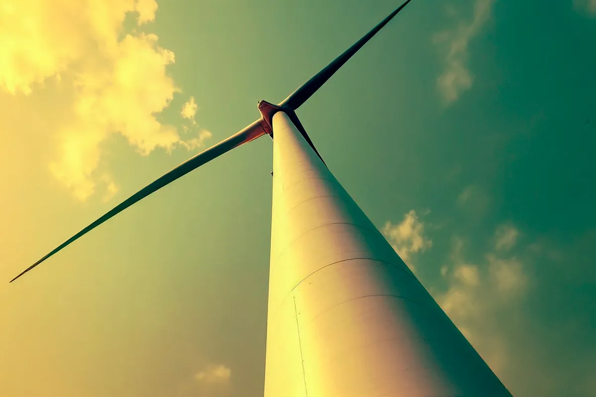 O que é transição energética e por que se fala tanto sobre isso? 29 Vista de baixo para cima de uma turbina eólica contra o céu colorido, simbolizando geração de energia renovável e sustentabilidade.