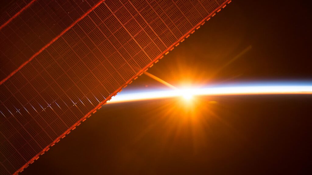 Painel solar em órbita diante do nascer do Sol sobre a Terra