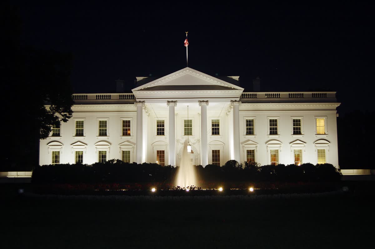 Casa Branca iluminada à noite, contexto visual para anúncio presidencial sobre força-tarefa de inteligência artificial